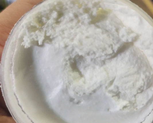 A close-up of an opened container filled with Grass-Fed Tallow Beard, Facial, and Body Scrub. The texture appears smooth and whipped, with some uneven areas on the surface, enhanced by essential oil blends from Crushed Botanicals Apothecary.