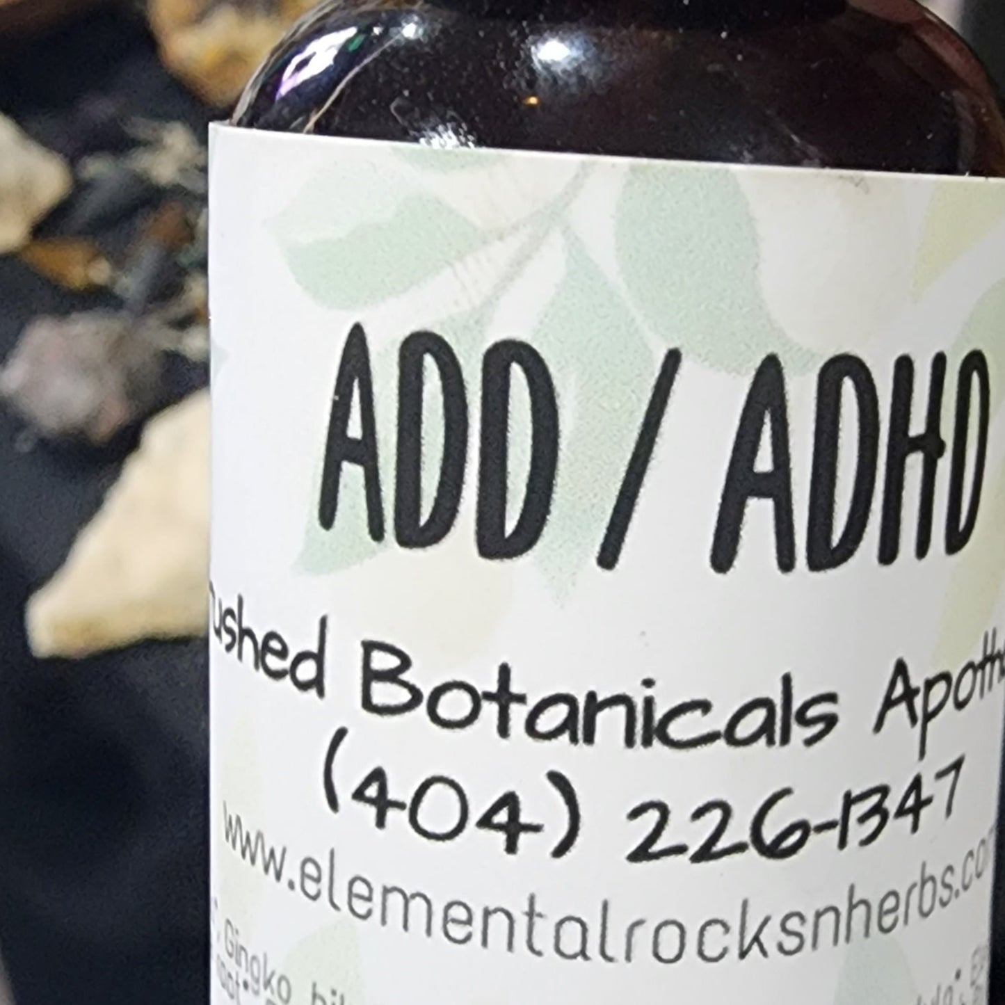 A small brown bottle labeled "ADD / ADHD Extract" from Crushed Botanicals Apothecary, designed to aid focus and concentration. Contact information and website visible. Ingredients include Ginkgo biloba, Lemongrass, Peppermint, and others. The 1 oz (28 ml) bottle is perfect for those seeking mental clarity.